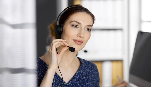 Femme d'affaires asiatique ou latino-américaine parlant par casque pendant qu'elle est assise au bureau. Centre d'appels et divers groupes de personnes en affaires — Photo