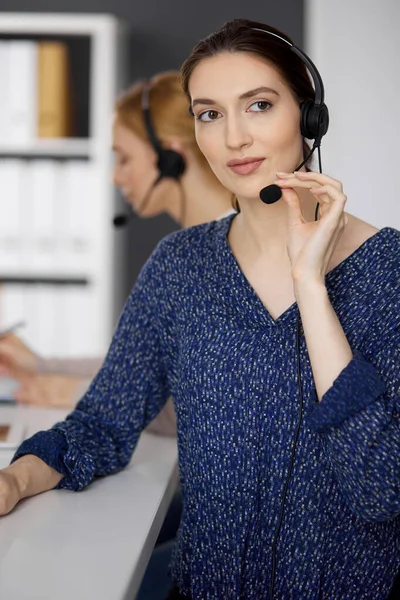 Empresaria asiática o latinoamericana hablando por auriculares mientras está sentada en el cargo. Centro de llamadas y grupo de personas diversas en los negocios — Foto de Stock