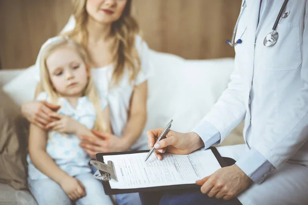 Doctor y paciente. Pediatra usando portapapeles mientras examina a la niña con su madre en casa. Niña enferma e infeliz en el examen médico. Concepto de medicina —  Fotos de Stock