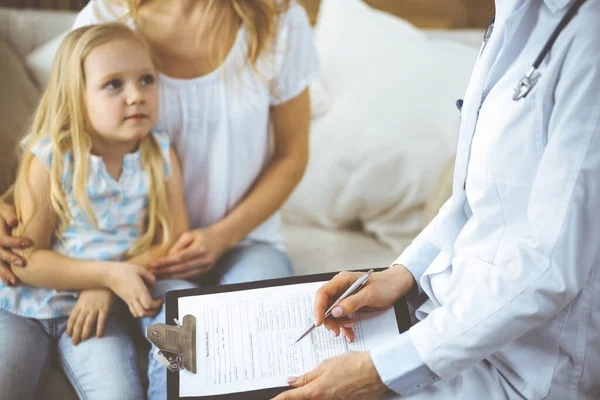 Doutor e paciente. Pediatra usando prancheta enquanto examina a menina com sua mãe na clínica em casa. Feliz bonito criança caucasiana no exame médico. Conceito de medicina — Fotografia de Stock