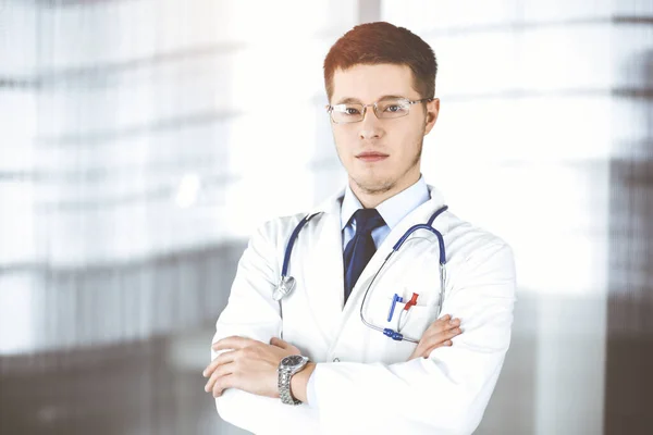 Dottore uomo, con occhiali e stetoscopio, è in piedi presso il suo soleggiato ufficio ospedaliero. Servizio medico perfetto in clinica. Buon futuro in medicina e sanità — Foto Stock