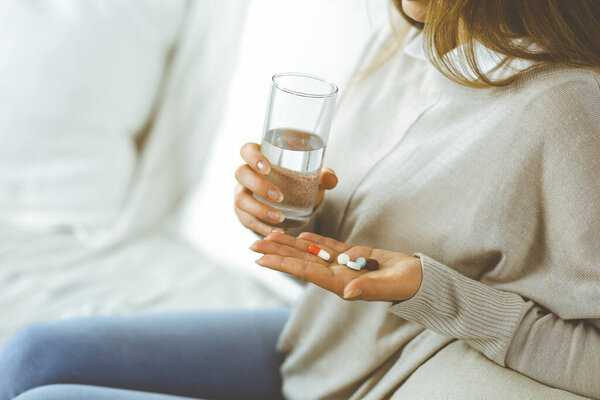 Close-up woman holding pills time to take medications, cure for headache, high blood pressure pain killer drugs at home. Stay at home concept during Coronavirus pandemic