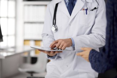 Bilinmeyen sakallı doktor ve hasta kadın tablet bilgisayarı kullanırken sağlık muayenesini tartışıyorlar, yakın plan. Tıp konsepti