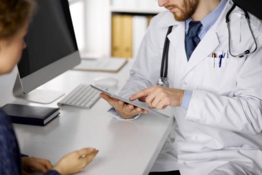 Bilinmeyen sakallı doktor ve hasta kadın tablet bilgisayarı kullanırken sağlık muayenesini tartışıyorlar, yakın plan. Tıp konsepti
