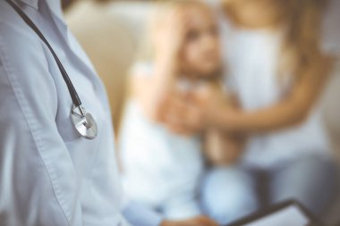 Doktor ve hasta. Pediyatrist, annesiyle birlikte küçük kızı muayene ederken pano kullanıyor. Sağlık muayenesinde hasta ve mutsuz bir çocuk. Tıp konsepti