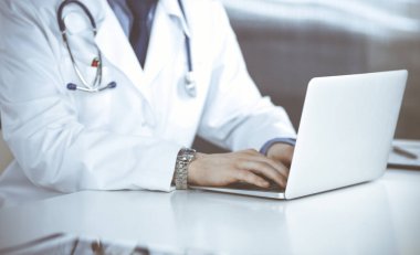 Bilinmeyen bir erkek doktor klinikte dizüstü bilgisayarla yakın planda çalışıyor. İşteki genç doktor. Mükemmel sağlık hizmeti, tıp konsepti