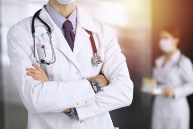 Güneşli klinikte kolları çapraz duran koruyucu maskeli kimliği belirsiz erkek doktor. Coronavirüs salgını sırasında ilaç kavramı