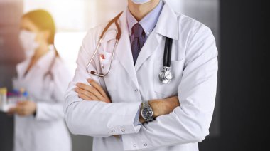 Güneşli klinikte kolları çapraz duran koruyucu maskeli kimliği belirsiz erkek doktor. Coronavirüs salgını sırasında ilaç kavramı
