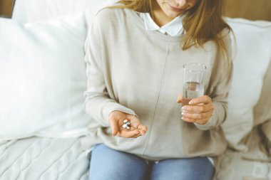Yakın plan kadın hapları tutuyor, ilaç alıyor, baş ağrısını tedavi ediyor, yüksek tansiyon ilaçları evde. Coronavirus salgını sırasında evde konsept kal