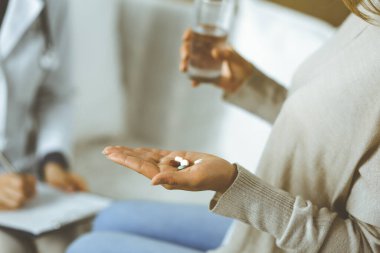 Yakın plan kadın-hasta doktorunun yanında haplar tutuyor. İlaç alma, baş ağrısı veya ağrı kesici ilaçların tedavisi için zaman var. Coronavirus salgını ve kendini izolasyon süresince evde kal.
