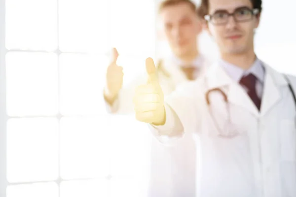 Two male doctors standing as a team and showing thumbs up as a symbol of the best service for patients in sunny clinic. Medicine concept — Stock Photo, Image