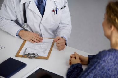 Bilinmeyen sakallı doktor ve hasta kadın güneşli klinikte otururken sağlık muayenesini tartışıyorlar. Yakın plan. Tıp konsepti