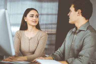 Yeşil gömlekli arkadaş canlısı genç işadamı ve programcı, modern bir ofiste masa başında bayan bir meslektaşla birlikte otururken bilgisayar üzerinde çalışıyor. Kadınlara odaklan. Başarılı olma kavramı