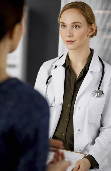 Amigável sorridente médico e paciente mulher discutindo exame de saúde atual enquanto sentado na clínica. Serviço médico perfeito no hospital. Conceito de medicina — Fotografia de Stock