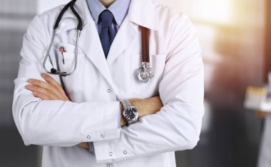 Güneşli klinikte kolları çapraz duran koruyucu maskeli kimliği belirsiz erkek doktor. Coronavirüs salgını sırasında ilaç kavramı