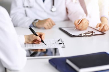 Bilinmeyen bir grup doktor masanın başında oturmuş güneşli hastane ofisinde hastalıkların tedavisini tartışıyorlar. Covid 2019