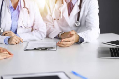 Erkek meslektaşı olan bilinmeyen kadın-doktor güneşli klinikteki masada otururken hastaya danışıyor, yakın plan. Covid 2019