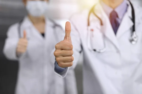 Onbekende man-dokter en vrouw staan recht als een team met duimen omhoog in de zonnige kliniek. Medicijnconcept tijdens de Coronavirus pandemie. Covid 2019 — Stockfoto