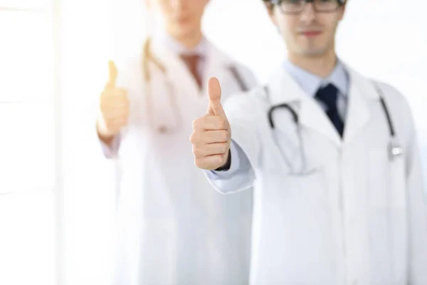 Due medici di sesso maschile in piedi come una squadra e mostrando pollici in su come simbolo del miglior servizio per i pazienti in clinica soleggiata. Concetto di medicina — Foto Stock