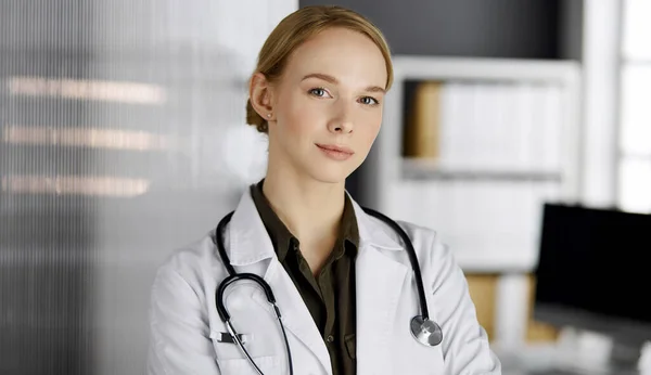 Friendly smiling female doctor standing in clinic. Portrait of friendly physician woman. Perfect medical service in hospital