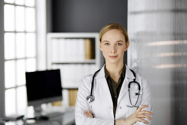 Friendly smiling female doctor standing in clinic. Portrait of friendly physician woman. Perfect medical service in hospital