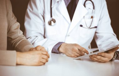 Bilinmeyen erkek doktor ve hasta kadın klinikte oturup tablet bilgisayar kullanırken bir şeyler tartışıyorlar. Hastanedeki en iyi sağlık hizmeti, ilaç, salgın durdurma.