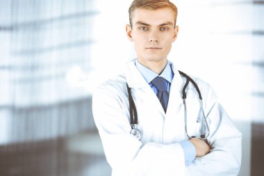 Doktor adam, steteskoplu, güneşli hastane ofisinde duruyor. Klinikte mükemmel bir tıbbi hizmet. Tıp ve sağlık sektöründe mutlu bir gelecek