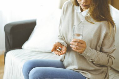 Yakın plan kadın hapları tutuyor, ilaç alıyor, baş ağrısını tedavi ediyor, yüksek tansiyon ilaçları evde. Coronavirus salgını sırasında evde konsept kal