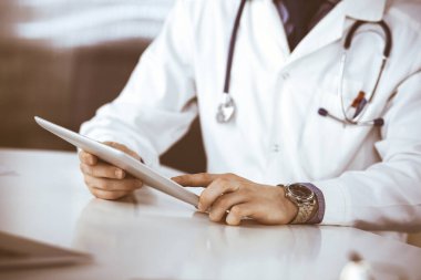 Bilinmeyen erkek doktor klinikteki tablet bilgisayarla yakın planda çalışıyor. İşteki genç doktor. Mükemmel sağlık hizmeti, tıp konsepti