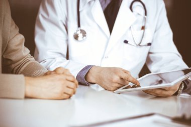Bilinmeyen erkek doktor ve hasta kadın klinikte oturup tablet bilgisayar kullanırken bir şeyler tartışıyorlar. Hastanedeki en iyi sağlık hizmeti, ilaç, salgın durdurma.