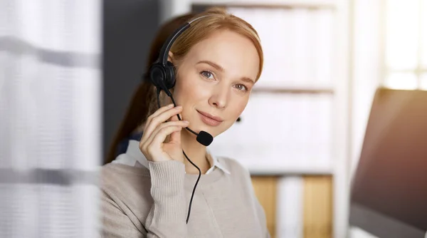 Amicale femme d'affaires caucasienne parlant par casque dans un bureau ensoleillé. Centre d'appels et divers groupes de personnes en affaires — Photo