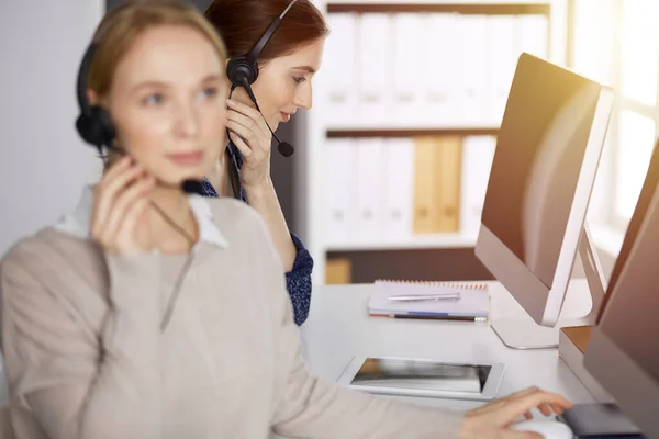 Mulher de negócios caucasiana amigável falando por fone de ouvido no escritório ensolarado. Call center e grupo de pessoas diversas em negócios — Fotografia de Stock