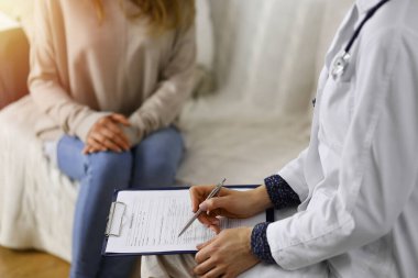 Kadın-doktor ve hasta yakın plan çekimleri. İçeride otururken sağlık muayenesini tartışıyorlar. Coronavirus salgını ve kendini izolasyon karantinası sırasında evde kal. Covid 2019