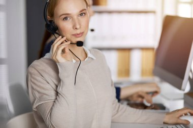 Kafkasyalı dost canlısı iş kadını güneşli ofiste kulaklıkla konuşuyor. Çağrı merkezi ve çeşitli iş grupları