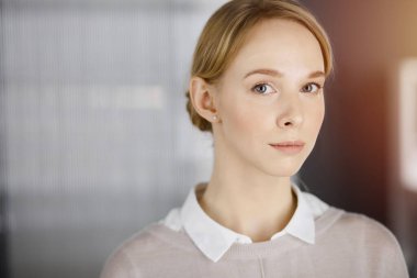 Dost canlısı, sıradan giyinmiş iş kadını güneşli ofiste dikiliyor. İş vesikalığı