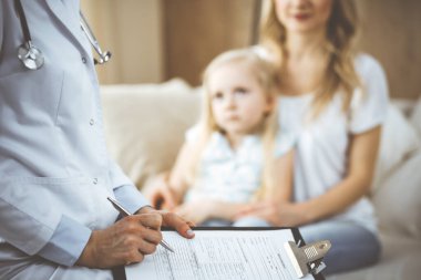 Doktor ve hasta. Pediyatrist, annesiyle birlikte küçük kızı muayene ederken pano kullanıyor. Sağlık muayenesinde hasta ve mutsuz bir çocuk. Tıp konsepti