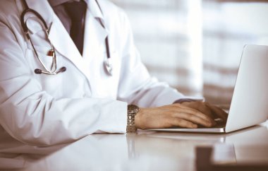 Bilinmeyen bir erkek doktor klinikte dizüstü bilgisayarla yakın planda çalışıyor. İşteki genç doktor. Mükemmel sağlık hizmeti, tıp konsepti