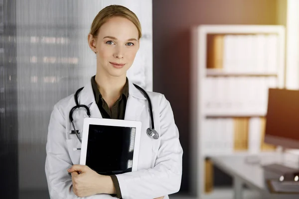 Amichevole medico femminile sorridente utilizzando tablet computer in clinica soleggiata. Una dottoressa al lavoro. Servizio medico perfetto in ospedale. Concetto di medicina — Foto Stock