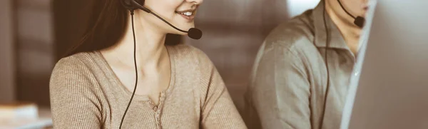 Deux jeunes dans des casques d'écoute parlent aux clients, assis au bureau. Concentre-toi sur la femme. Opérateurs de centre d'appels au travail — Photo