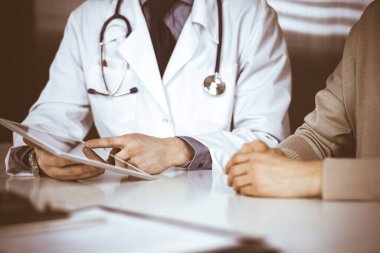 Bilinmeyen erkek doktor ve hasta kadın klinikte oturup tablet bilgisayar kullanırken bir şeyler tartışıyorlar. Hastanedeki en iyi sağlık hizmeti, ilaç, salgın durdurma.