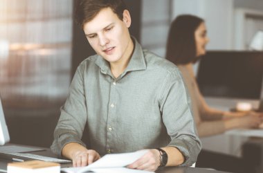 Bilgisayarında çalışan genç bir işadamı ofisteki masada oturuyor. Bir adamın portresi.