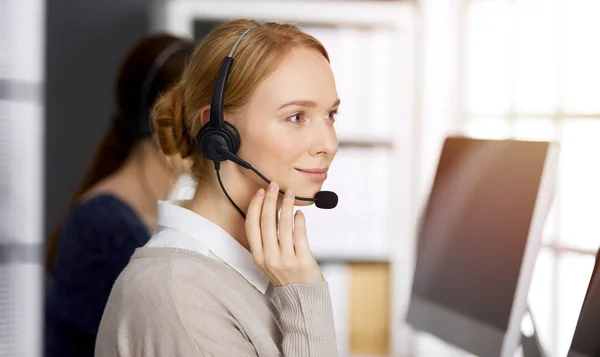 Amicale femme d'affaires caucasienne parlant par casque dans un bureau ensoleillé. Centre d'appels et divers groupes de personnes en affaires — Photo