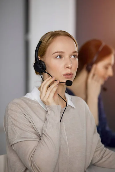 Amicale femme d'affaires caucasienne parlant par casque dans un bureau ensoleillé. Centre d'appels et divers groupes de personnes en affaires — Photo