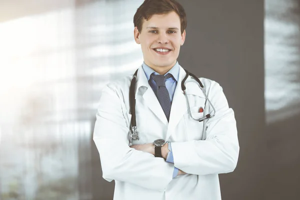 Un jeune médecin positif sourit à la caméra. Portrait de médecin professionnel en clinique ensoleillée — Photo