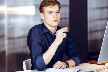 Genç sarışın işadamı iş yerinde bilgisayarla strateji düşünüyor. Girişim işi, başarı için çok çalışmak ve zamanın dışında çalışmak demektir.