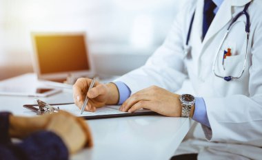 Bir doktor, hastanedeki güneşli dolapta birlikte otururken hastasıyla konuşuyor. Doktor ilaç kayıtlarını doldurmak için pano kullanıyor. Mükemmel tıbbi servis.