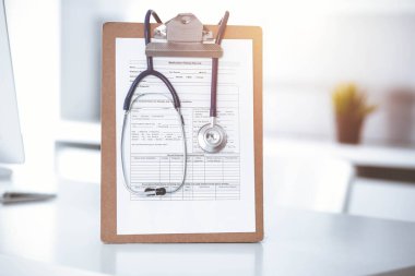 Üzerinde ilaç geçmişi olan steteskop ve dosya güneşli doktorların çalıştığı yerde masada. Tıp konsepti