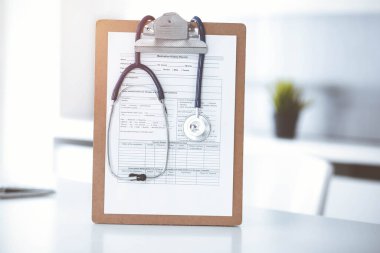 Üzerinde ilaç geçmişi olan steteskop ve dosya güneşli doktorların çalıştığı yerde masada. Tıp konsepti