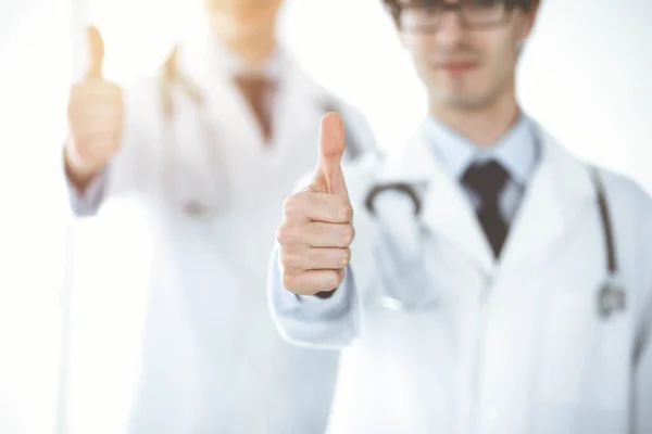 한 팀으로 서 있는 두 명의 남성 의사들 이 양지바른 병원의 환자들을 위한 최고의 서비스의 상징으로 엄지손가락을 보여 주고 있습니다. 의학적 개념 — 스톡 사진