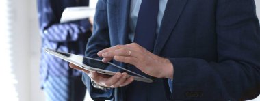 İş adamı şirket toplantısı sırasında dijital tablet hakkında bilgi kontrol ediyor, iş arkadaşlarıyla işbirliği yapıyor ve modern iletişim ve takım çalışması için teknoloji kullanıyor